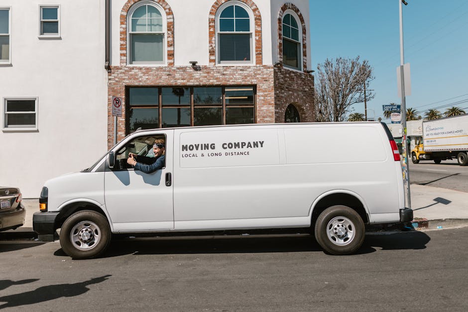 Inside the back of a white delivery van used for house removals, two workers from Man with Van Woolwich are loadings boxes and packaging materials. The woman on the left, wearing a cap, glasses, and a