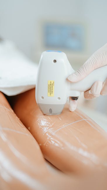 A close-up view of a person receiving a medical or aesthetic treatment, with a gloved hand holding a handheld device that is being applied to a person's skin. The device emits a gentle light or laser and is positioned on a smooth, exposed area of skin, which appears to be the thigh or buttock. The person receiving the treatment is lying on a surface covered with protective paper or plastic wrap, suggesting a clinical or professional setting. In the background, there is a blurred monitor or screen with a light blue hue, indicating the use of specialized equipment during a home relocation or professional moving service, such as packing or preparation for transport, depicted in the context of the services provided by Man with Van Woolwich.